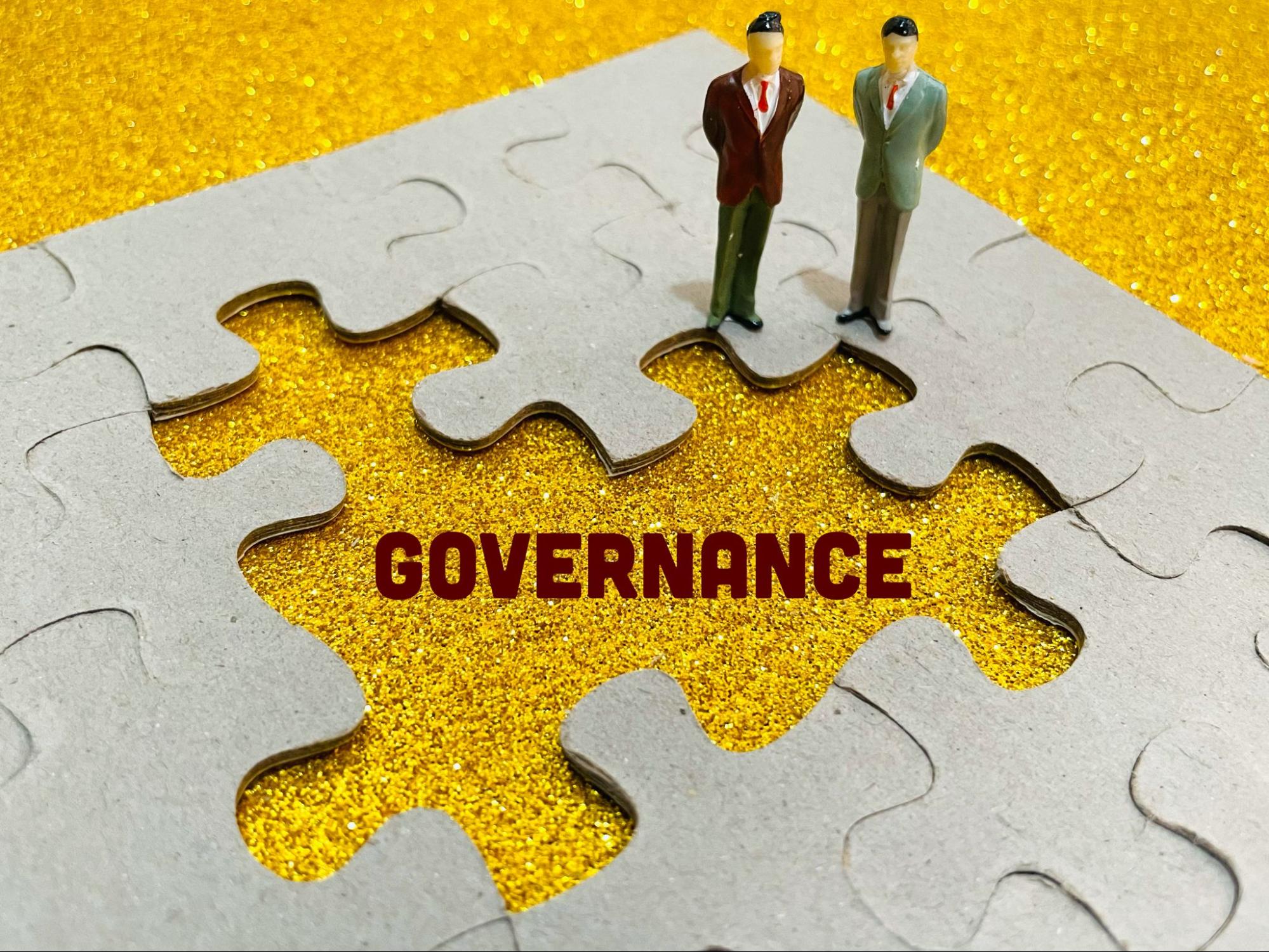 Two businessman figurines stand on top of a puzzle with the word 'Governance' in the center with missing pieces, symbolizing its significance to the company..