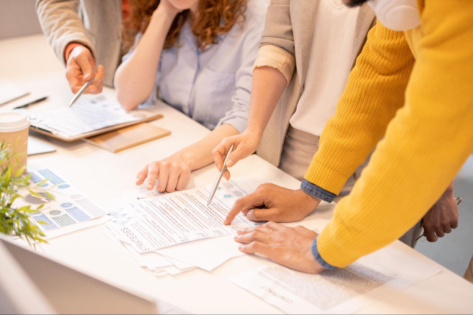 Close-up of four unrecognizable business woman standing at a table, reviewing and discussing the business registration procedure with the forms in front of them.