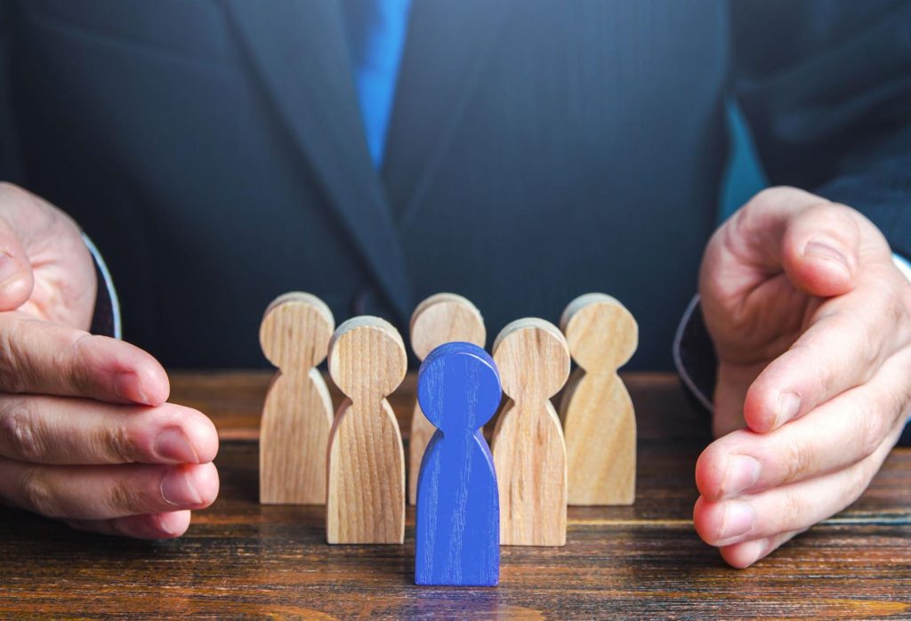 A close-up of a company leader's hand arranging wooden mini dolls to represent building an effective team, symbolizing organizational governance.