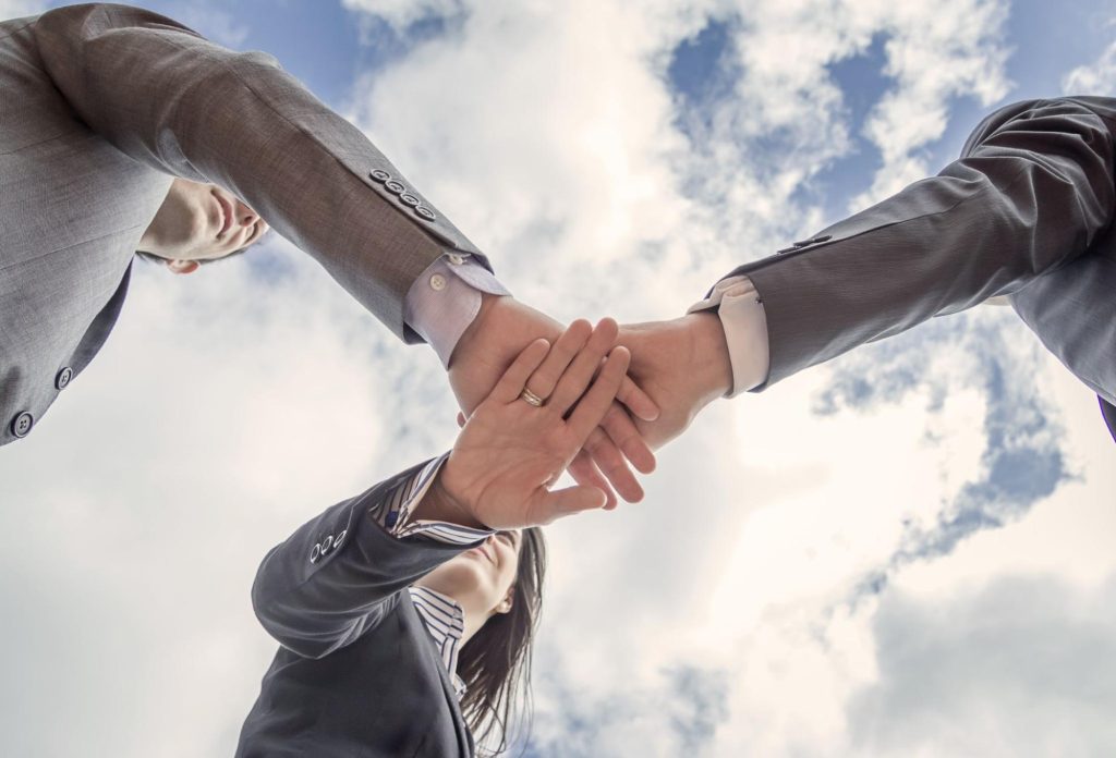 A bottom view of a business team showing unity with hands together over a blue sky.
