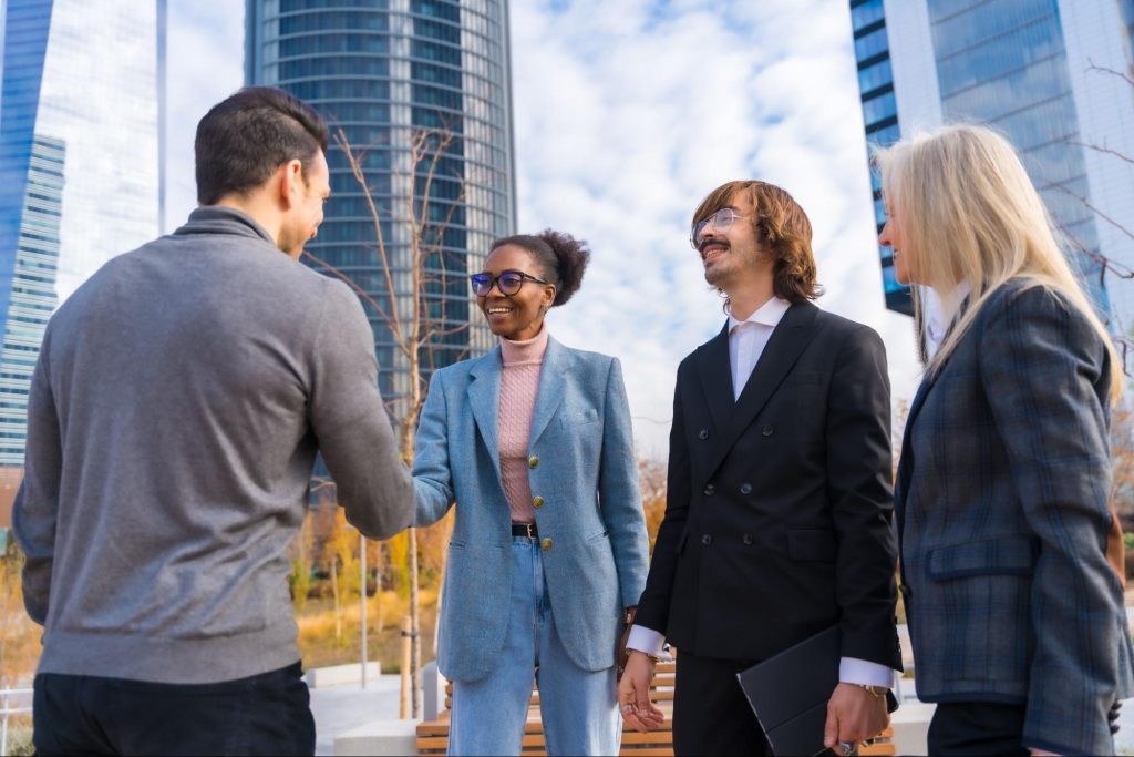 Business people talking and shaking hands outside office buildings. 