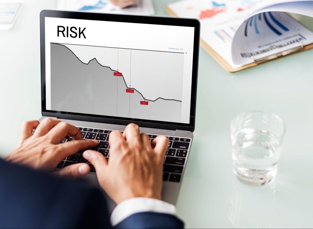 Word “risk” on a computer screen with a graph next to a cup of water and a clipboard. 
