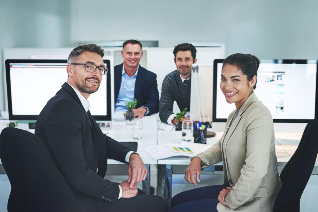 Three male and one female sitting at a desk with computer monitors. 