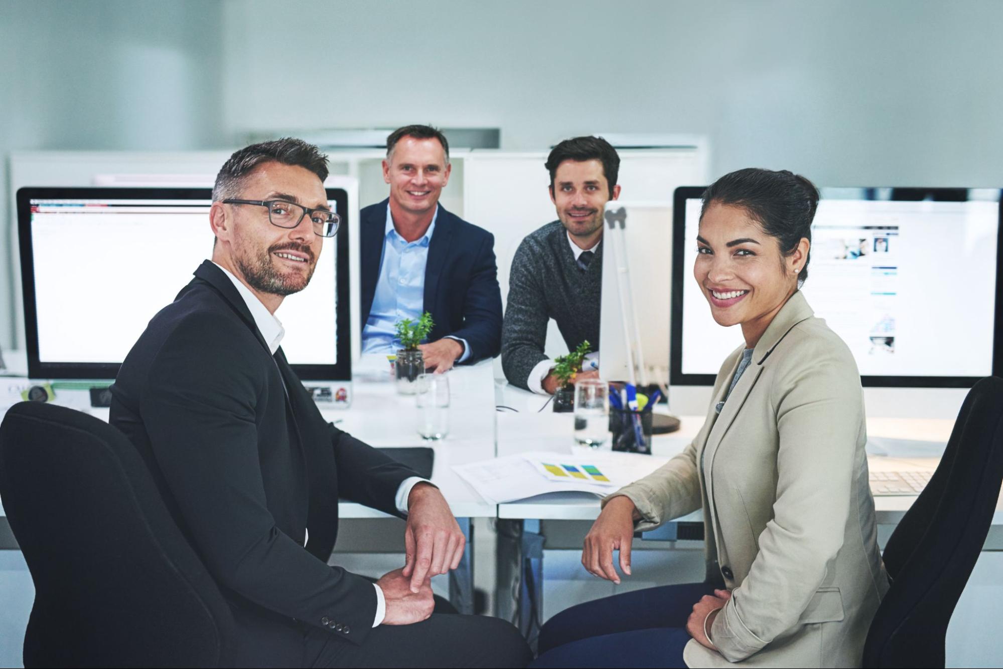 Three male and one female sitting at a desk with computer monitors.